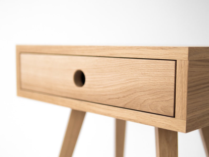 May include: A light wood bedside table with a single drawer and tapered legs. The drawer has a round cutout for a handle.