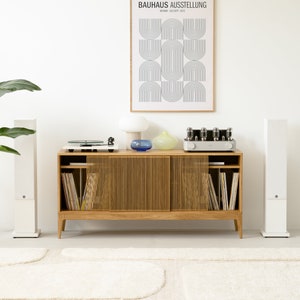 Puede incluir: Un armario de madera de estilo moderno de mediados de siglo con puertas correderas, que incluye un tocadiscos, un amplificador vintage y dos altavoces blancos. El armario est&aacute; decorado con un p&oacute;ster enmarcado que dice "BAUHAUS AUSSTELLUNG WEIMAR, 20. AUG. - SEPT. 1923".