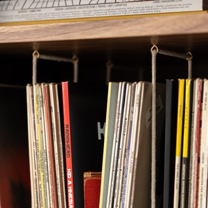 May include: A wooden shelf displays a collection of vinyl records and magazines. The records are in various colors, with titles like "Radiohead" and "Kid A Mnesia" visible. A magazine with the text "LABEL-MAGAZINE.COM" is on top.