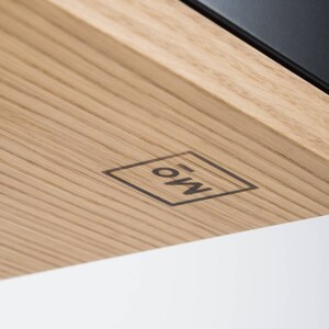 Puede incluir: Primer plano de una superficie de madera con un logotipo en blanco y negro que dice "EOW" dentro de un cuadrado.