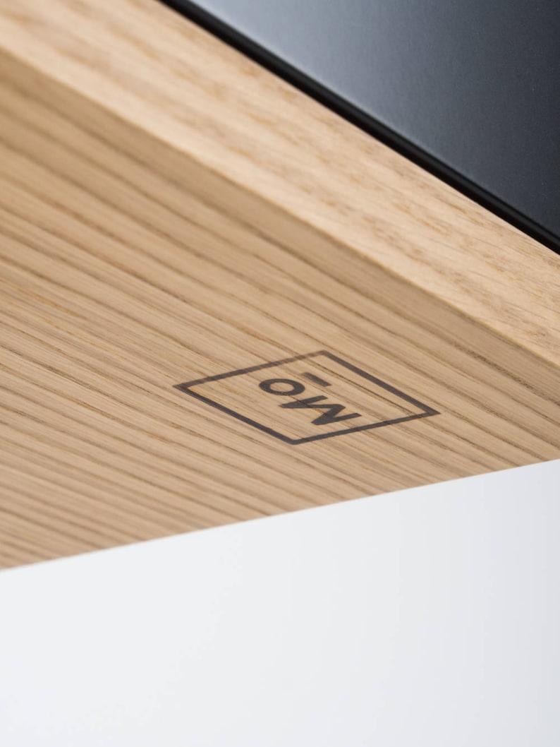 Puede incluir: Primer plano de una superficie de madera con un logotipo en blanco y negro que dice "EOW" dentro de un cuadrado.