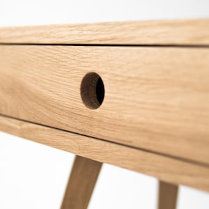 May include: A light wood bedside table with a single drawer and a round knob. The bedside table has a simple, modern design and is ideal for a bedroom.