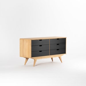 May include: A six-drawer dresser with black drawers and a light wood frame. The dresser has tapered legs and a mid-century modern style.