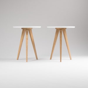May include: Two white round tables with wooden tripod legs. The tables are on a white background.