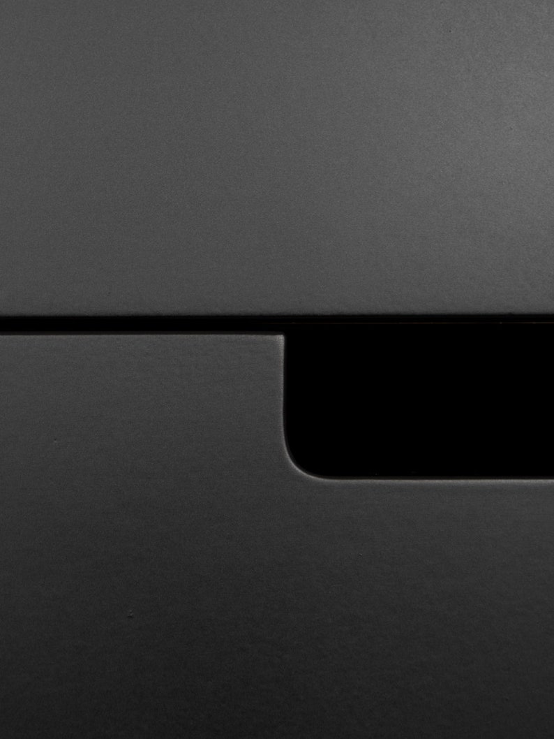 May include: A close-up of a black drawer with a small, rectangular cutout in the front.