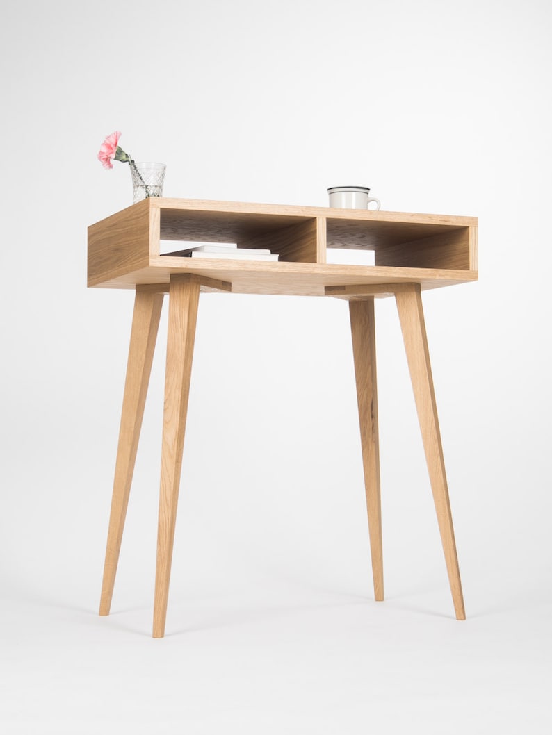 May include: A light wood console table with two shelves and four tapered legs. A pink carnation in a glass vase and a white ceramic mug are on the top shelf.