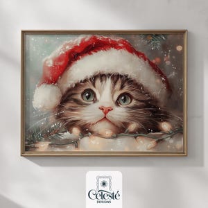 May include: A framed print featuring a fluffy cat wearing a Santa hat. The cat has blue eyes and is surrounded by Christmas lights and pine needles. The print has a gold frame and the Celeste Designs logo.