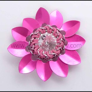 May include: A pink metal flower with a silver and pink chainmail centre and a clear crystal in the middle.