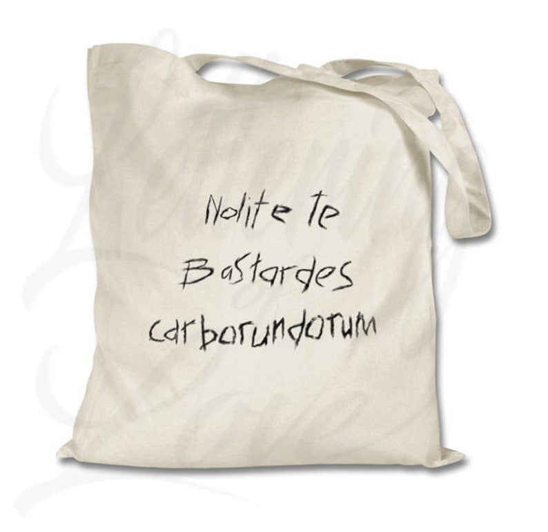 Pu&ograve; includere: Una borsa tote in tela bianca con testo scritto a mano in nero che recita "Nolite te Bastardes carborundum".