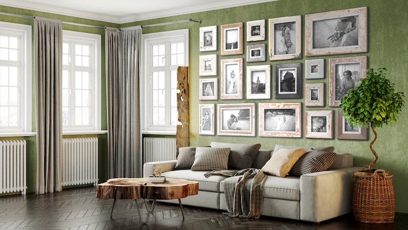 May include: A living room with a green wall adorned with framed black and white photos. A gray sofa with throw pillows and a blanket sits below the gallery wall. A wooden coffee table and a potted tree complete the cozy interior design.