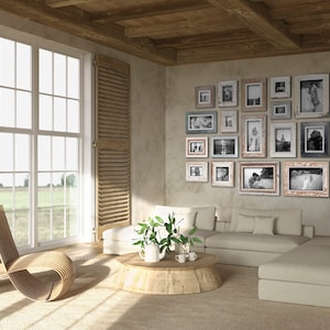May include: A living room with a neutral color palette, featuring a large window with wooden shutters and a collection of framed photographs on the wall. A wooden chair and a sectional sofa are also present.