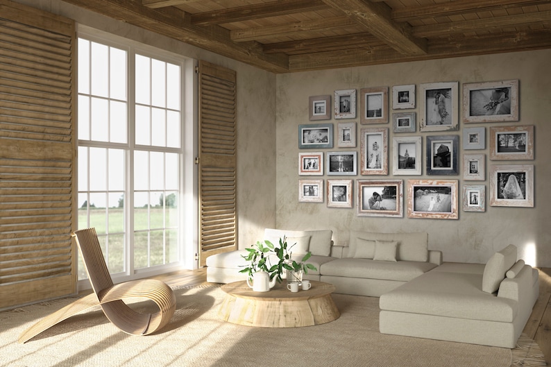 May include: A living room with a neutral color palette, featuring a large window with wooden shutters and a collection of framed photographs on the wall. A wooden chair and a sectional sofa are also present.