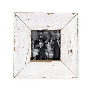 May include: Square, distressed white picture frame with a black and white photograph of a party. The frame has a rustic, weathered appearance with visible wood grain and peeling paint. The photograph shows people at tables with balloons.