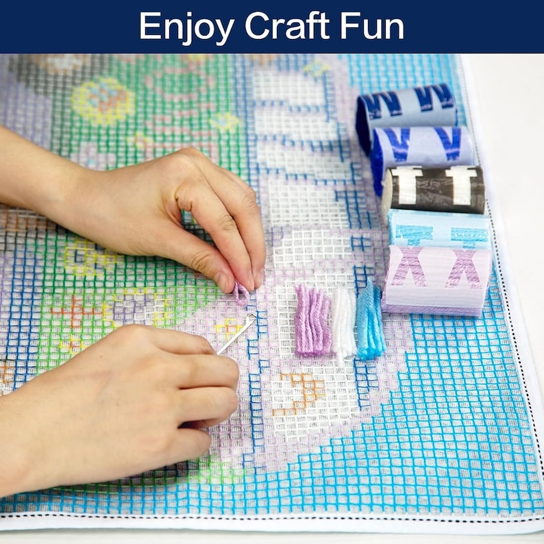 May include: A person is working on a colorful needlepoint project. The project is on a white gridded canvas with a blue border. The person is using a needle and yarn to create a design. There are several spools of yarn in different colors on the right side of the image.