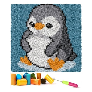 Könnte beinhalten: Ein blauer und weißer Teppich mit einem Cartoon-Pinguin-Design. Der Teppich besteht aus Garn und soll vom Benutzer fertiggestellt werden. Das Bild zeigt auch eine Vielzahl von farbigen Garnrollen und einen Haken.