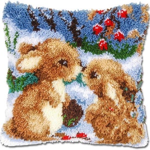 May include: A close-up of a needlepoint pillow featuring two brown rabbits in a snowy winter scene. The rabbits are looking at each other and there are red berries in the background.
