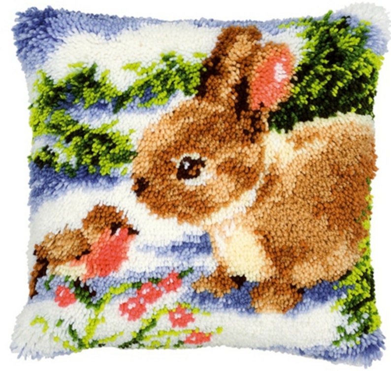 May include: A brown bunny with a pink ear sits in a snowy landscape with a red robin bird. The background is a blue and white winter scene with green trees and red berries.