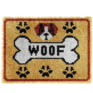 May include: A rectangular doormat with a tan background and a red border. The mat features a white bone shape with the word "WOOF" in black, a dog's head, and black paw prints. The mat has a fringed edge.