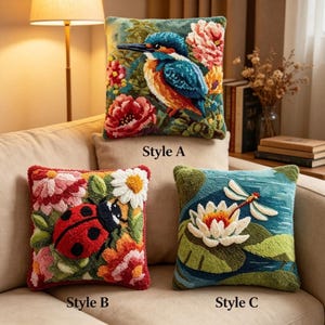 May include: Three square throw pillows with textured punch needle embroidery. Style A features a kingfisher and flowers. Style B shows a ladybug among daisies and blossoms. Style C depicts a dragonfly over a water lily and lily pads.