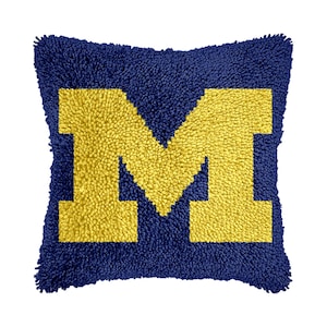 May include: A blue and yellow throw pillow with a large yellow "M" in the center.