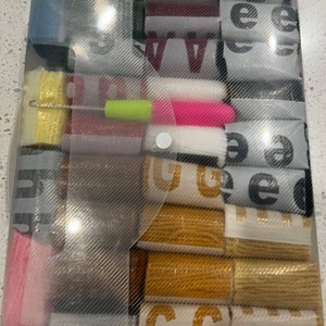 May include: A clear plastic storage box filled with various rolls of colorful fabric ribbon. The ribbon is in different colors, patterns, and widths. The box has a white handle.