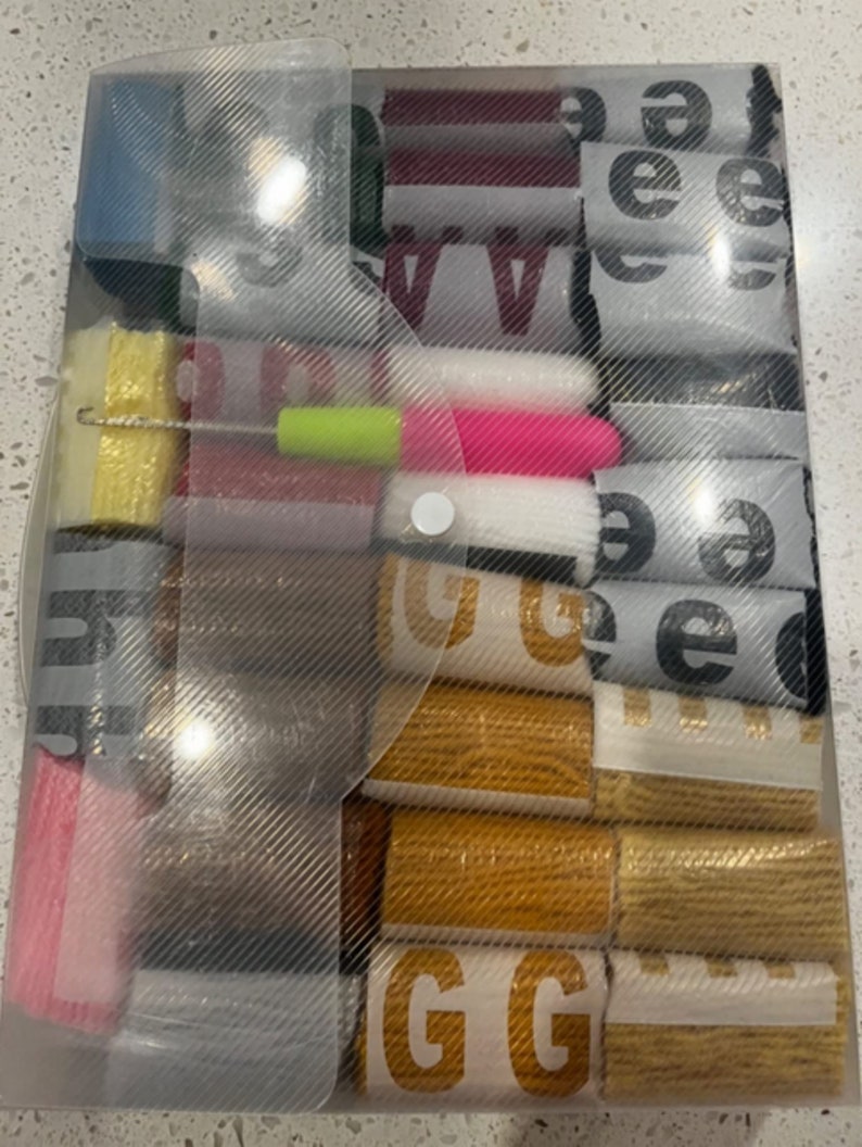 May include: A clear plastic storage box filled with various rolls of colorful fabric ribbon. The ribbon is in different colors, patterns, and widths. The box has a white handle.