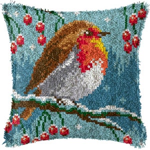 Könnte beinhalten: Quadratisches Zierkissen mit einem detaillierten, strukturierten Design eines Rotkehlchens auf einem schneebedeckten Ast. Der Vogel hat braune, orange und weiße Federn, vor einem blauen Hintergrund mit roten Beeren. Ein gemütliches Wohnaccessoire.