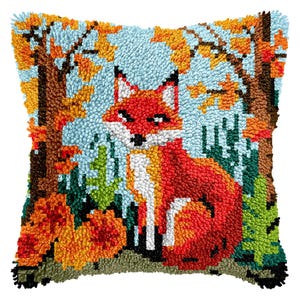 May include: A square, handmade pillow featuring a fox in a forest scene. The fox is red, white, and orange, set against a light blue background. The trees and foliage are in shades of brown, orange, and green.