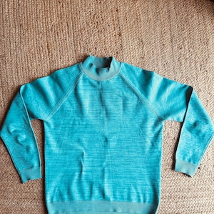 Op de afbeelding: Een tealblauwe mock neck trui met lange mouwen.