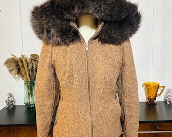 Puede incluir: Chaqueta de tweed marrón con capucha de piel sintética. La chaqueta tiene cierre de cremallera y se exhibe en un maniquí. La chaqueta es de color neutro y parece ser un abrigo de invierno.
