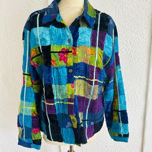 May include: A colourful patchwork jacket in blue, purple, green, and black. The jacket has a collared neckline, button-down front, and long sleeves. Floral and geometric patterns are incorporated. The jacket is displayed on a mannequin.