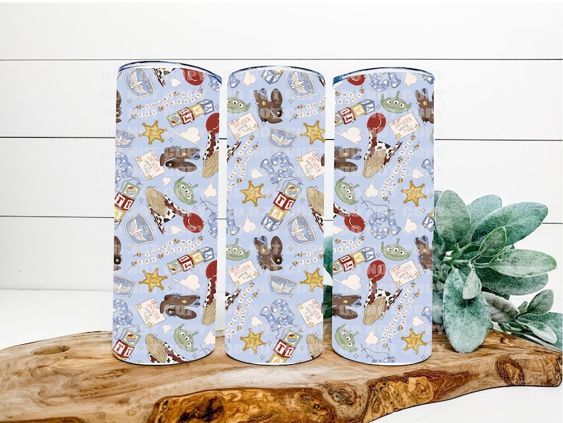 May include: Three cylindrical tumblers featuring a light blue background with a repeating pattern of cartoon characters, cowboy boots, sheriff stars, alphabet blocks, and small green aliens. The design includes various small icons and text elements.