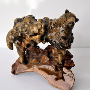 Peut inclure: Une sculpture en bois d'un ours debout sur un morceau de bois flotté. L'ours est sculpté dans un style réaliste et est de couleur brun et noir.