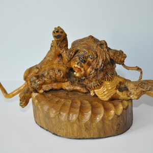 Peut inclure: Une sculpture en bois de deux chiens bruns jouant, l'un sur l'autre, sur une base en bois.