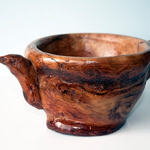 Peut inclure: Un bol en bois avec deux poignées en forme de tête d'oiseau. Le bol est en bois brun foncé avec un motif de grain naturel.