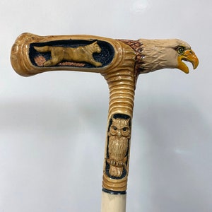 Peut inclure: Une canne en bois avec une tête d'aigle sculptée, un hibou sculpté et un loup sculpté sur la poignée.