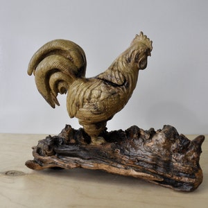 Peut inclure: Sculpture en bois d'un coq debout sur un morceau de bois flotté. Le coq est sculpté en détail et a une finition en bois naturel.
