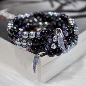 May include: A multi-strand bracelet with black, silver, and purple beads. The bracelet has two silver angel wing charms.