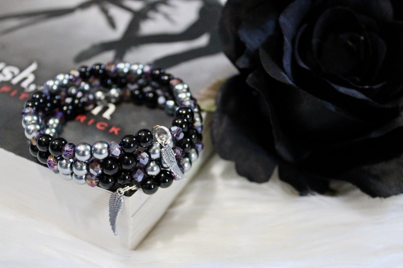 May include: A multi-strand bracelet with black, silver, and purple beads. The bracelet has two silver angel wing charms.
