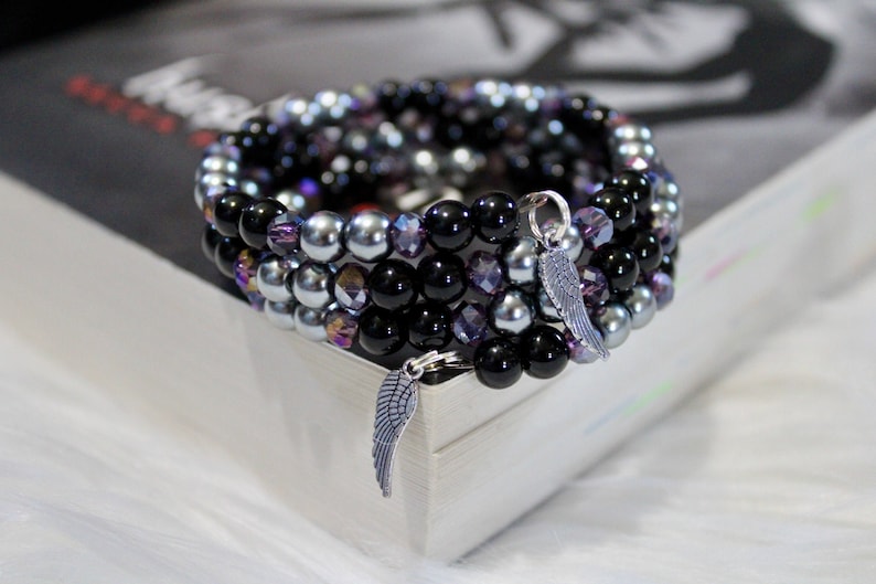 May include: A multi-strand bracelet with black, silver, and purple beads. The bracelet has two silver angel wing charms.