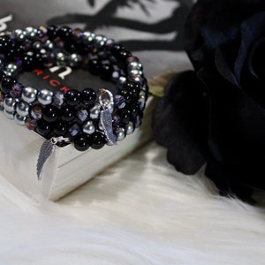 May include: A multi-strand bracelet with black, silver, and purple beads. The bracelet has a silver charm in the shape of a wing.