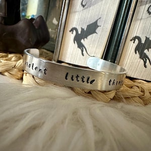 May include: Silver bracelet with the words "violent little things" engraved on it.