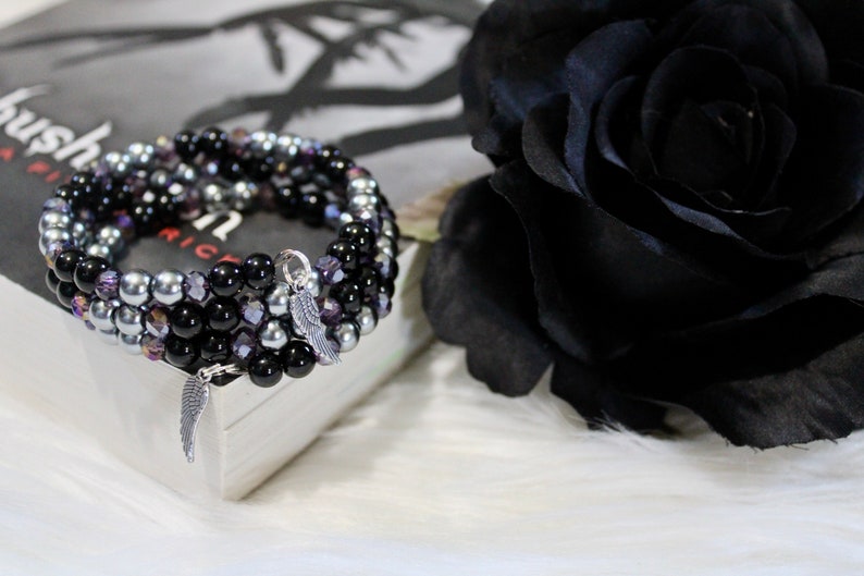 May include: A multi-strand bracelet with black, silver, and purple beads. The bracelet has two silver angel wing charms.
