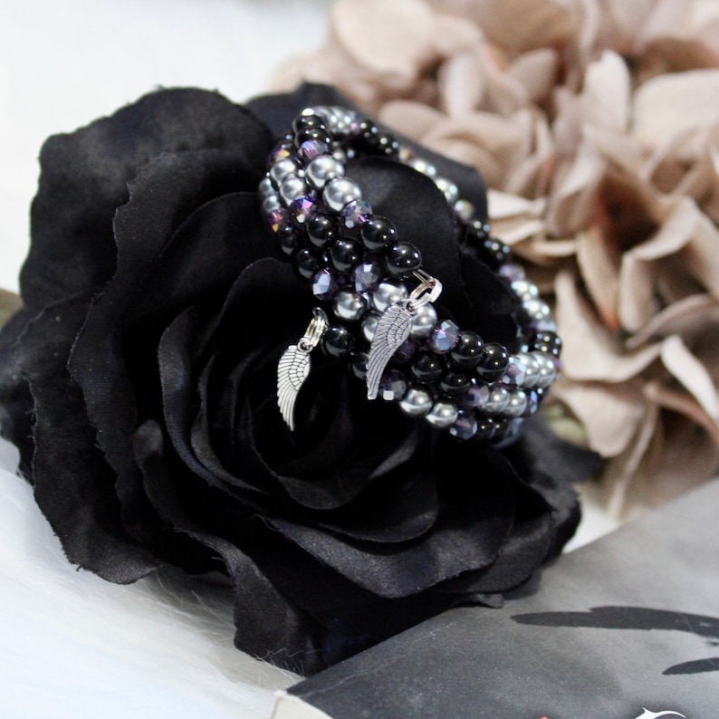May include: A set of three beaded bracelets with black, silver, and purple beads. Each bracelet has a small silver charm in the shape of a wing.