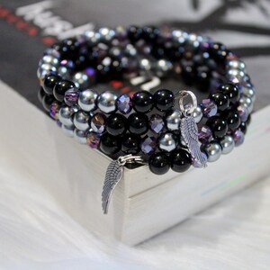 May include: A multi-strand bracelet with black, silver, and purple beads. The bracelet has a silver charm in the shape of a wing.