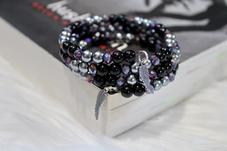 May include: A multi-strand bracelet with black, silver, and purple beads. The bracelet has a silver charm in the shape of a wing.