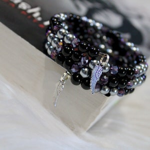 May include: A multi-strand bracelet with black, silver, and purple beads. The bracelet has two silver angel wing charms.