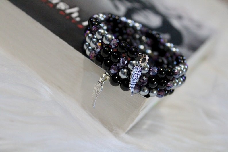 May include: A multi-strand bracelet with black, silver, and purple beads. The bracelet has two silver angel wing charms.