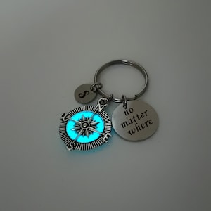 May include: A silver keyring with a glowing blue compass pendant, an initial charm, and a circular tag that reads "no matter where". The compass design features a star in the centre.