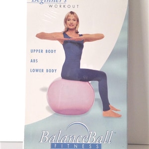May include: A fitness DVD titled "BalanceBall Fitness" with the text "Beginner's Workout." The cover shows a woman in blue workout attire on a pink exercise ball. The DVD is a special compilation sampler.